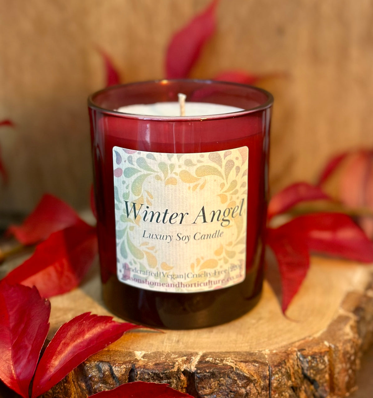 Soy wax candle labeled 'Winter Angel' on a wooden surface with red leaves
