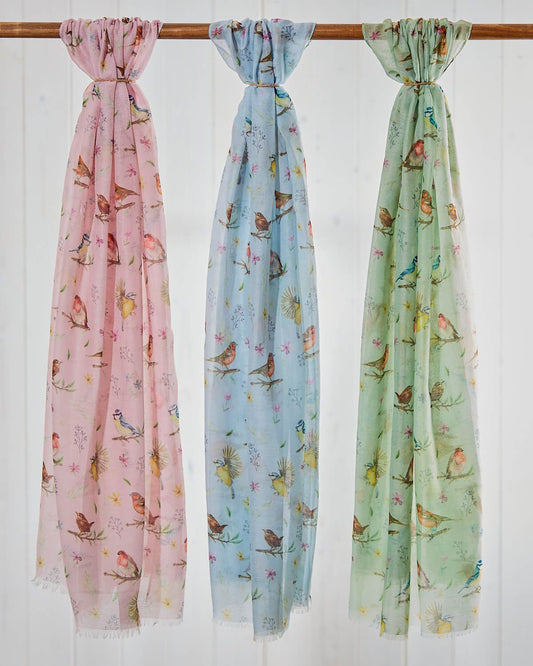 Three scarves with bird patterns in pink, blue, and green hanging on a rod.