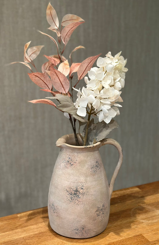Vintage-style pitcher with artificial flowers on a wooden surface