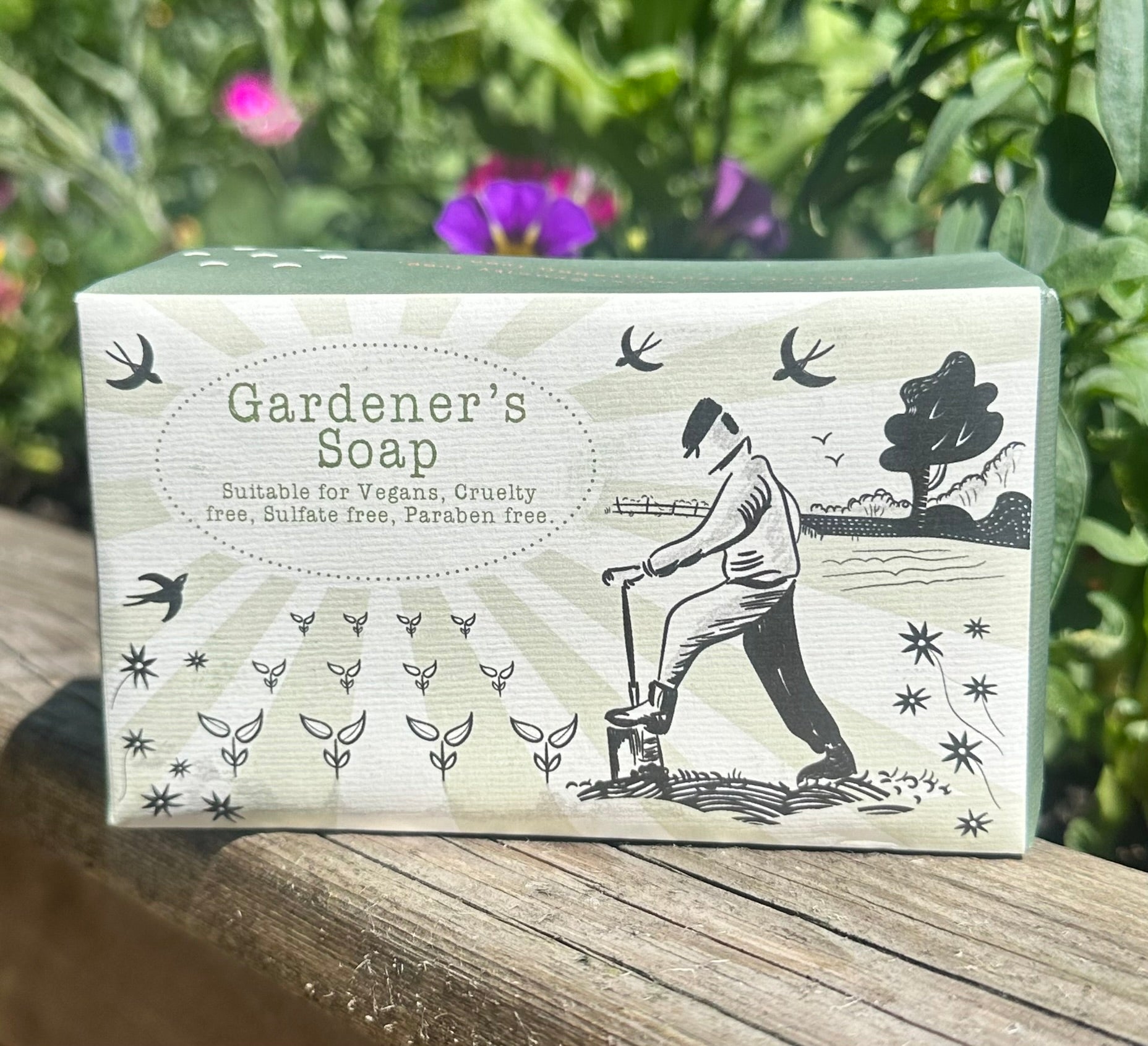 Natural Gardener’s Soap photographed in garden setting with colourful pansies and fresh herbs behind