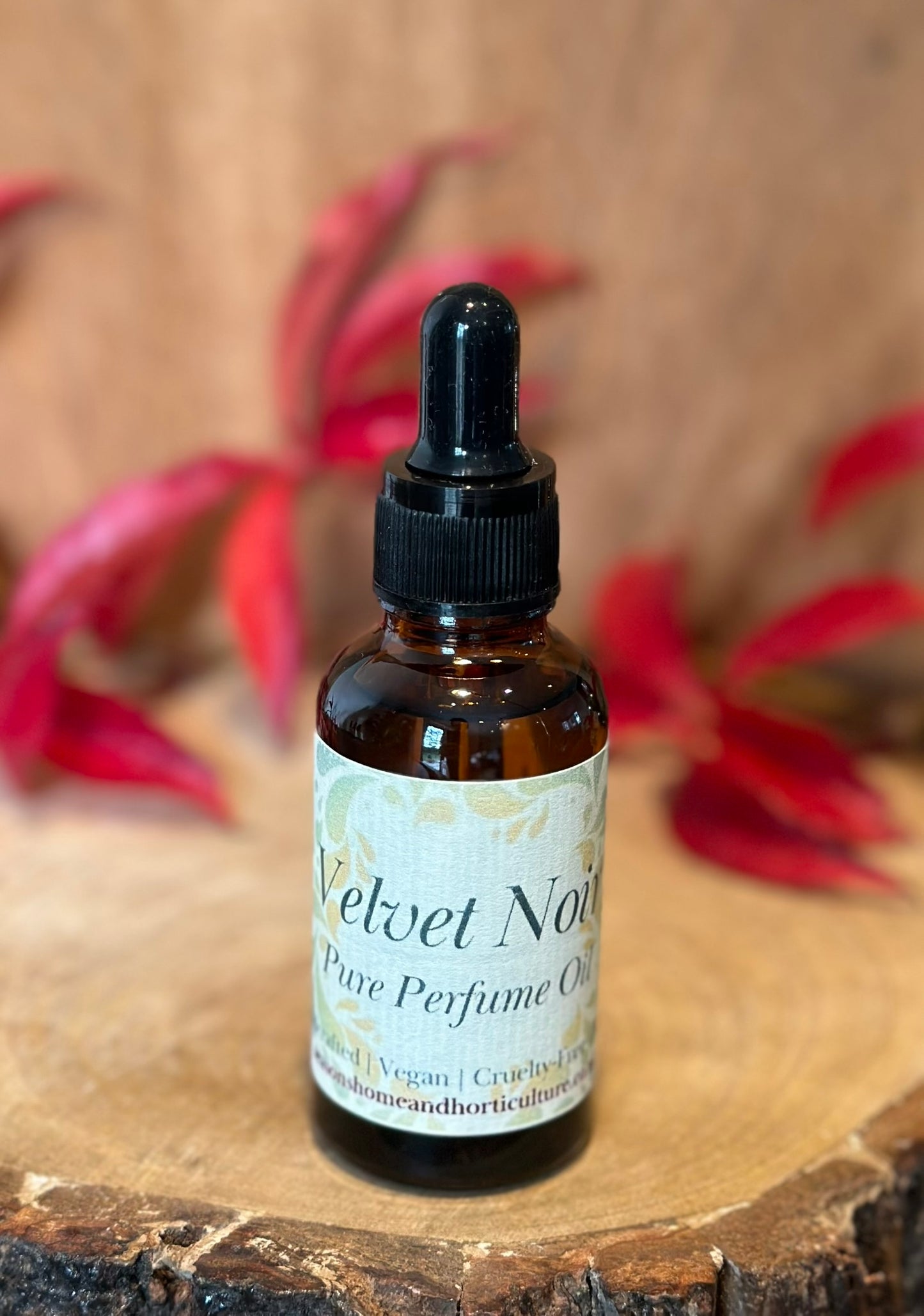 Bottle of Velvet Noir pure perfume oil on a wooden surface with red flowers in the background