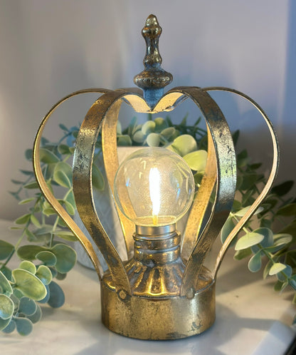 Decorative gold lamp with a light bulb inside, surrounded by green foliage.