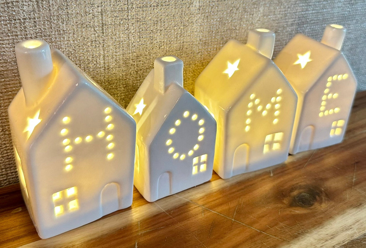 Set of white ceramic tealight houses spelling HOME with warm glowing lights — cosy decorative homeware perfect for Christmas or new home gifts.