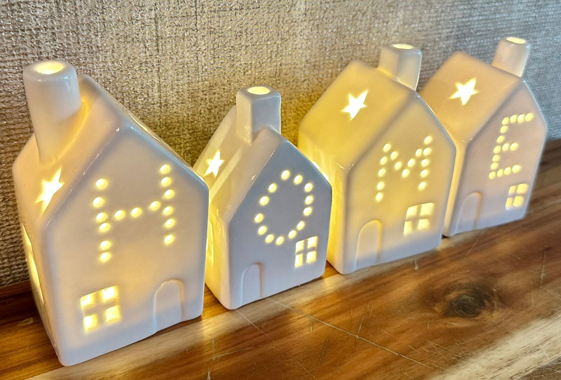 Set of white ceramic tealight houses spelling HOME with warm glowing lights — cosy decorative homeware perfect for Christmas or new home gifts.